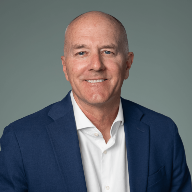 Professional headshot of Ed Messman, smiling and wearing a dark blazer and white shirt, posed against a neutral gray background.
