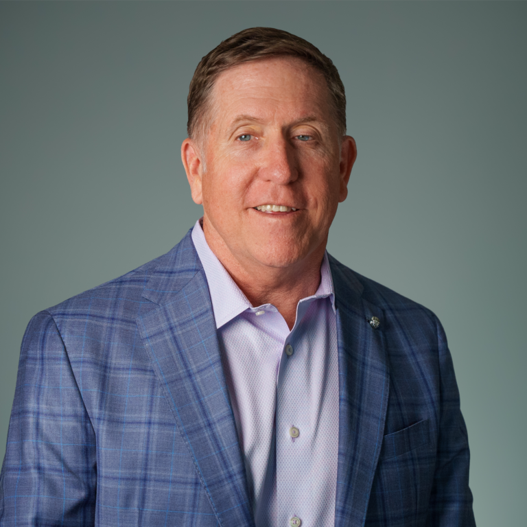 Professional headshot of Scott Rerucha, smiling and wearing a dark blazer and light-colored shirt, posed against a light gray background.